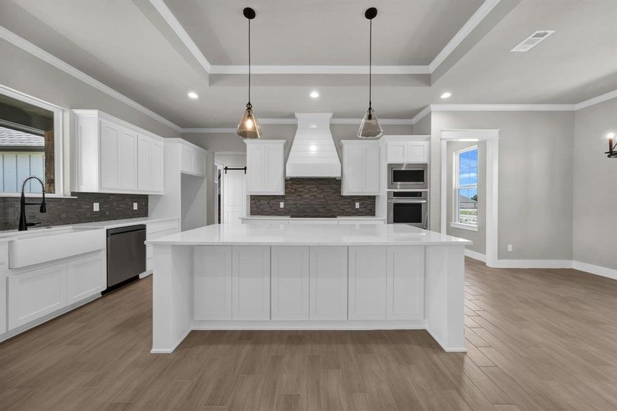 Kitchen with a raised ceiling, custom range hood, light hardwood / wood-style flooring, and appliances with stainless steel finishes, large eat at island with storage