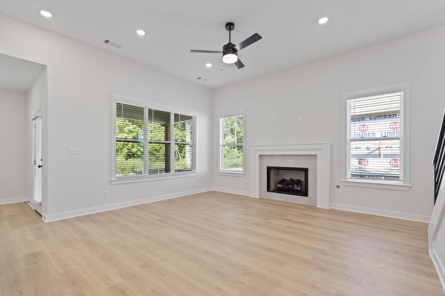 Spacious living area featuring wood-finish flooring, a contemporary fireplace with a classic mantel, abundant natural light from multiple windows, and recessed lighting