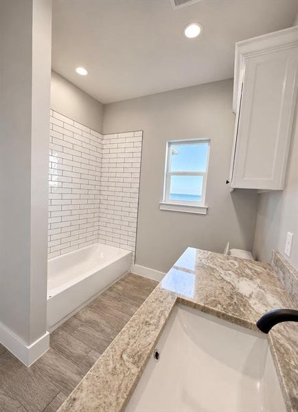 Bathroom featuring a white subway tile shower surround, a built-in bathtub, and wood-finish flooring Bathroom featuring a white subway tile shower surround, a built-in bathtub, and wood-finish flooring