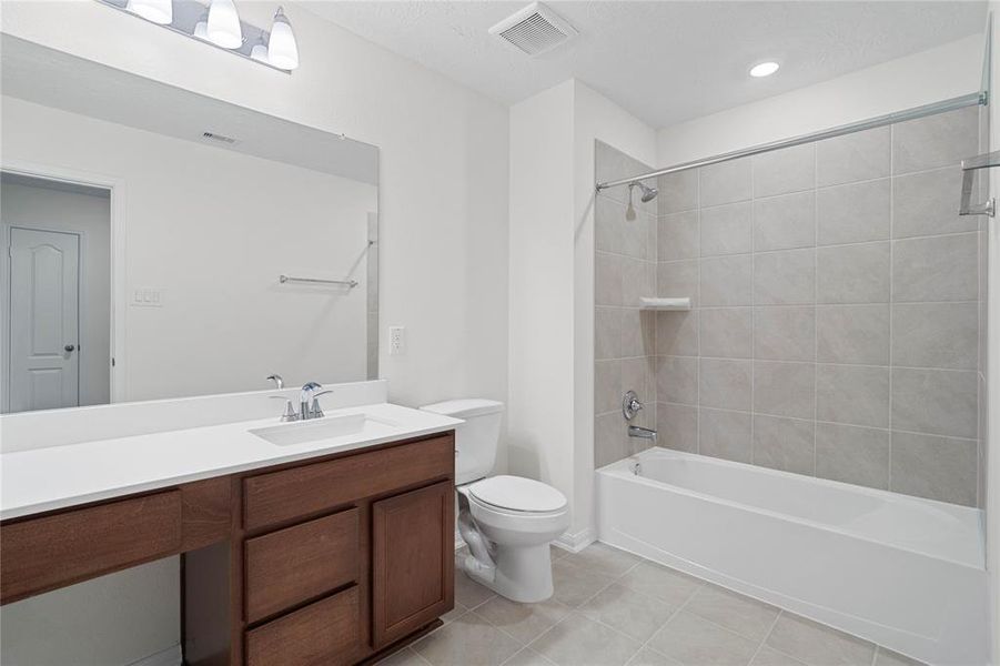 Secondary bath features tile flooring, bath/shower combo with tile surround, stained wood cabinets, beautiful light countertops, mirror, sleek fixtures and modern finishes.