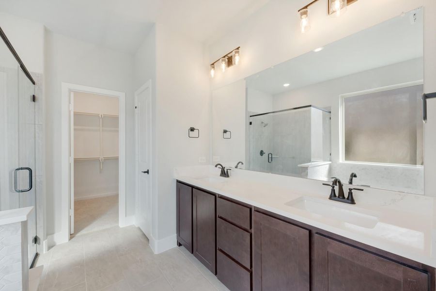 Master bathroom with double vanity, dark wood cabinets, glass shower, and walk-in closet entrance