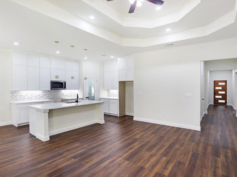 Kitchen with tasteful backsplash, a center island with sink, white cabinets, stainless steel microwave, and ornamental molding Kitchen with tasteful backsplash, a center island with sink, white cabinets, stainless steel microwave, and ornamental molding