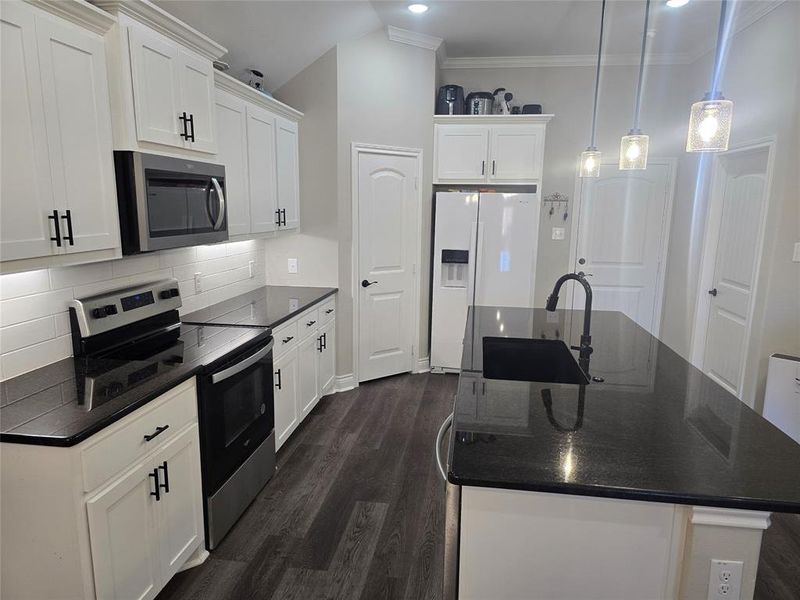 Kitchen with pendant lighting, white cabinets, stainless steel appliances, a center island with sink, and dark hardwood / wood-style flooring