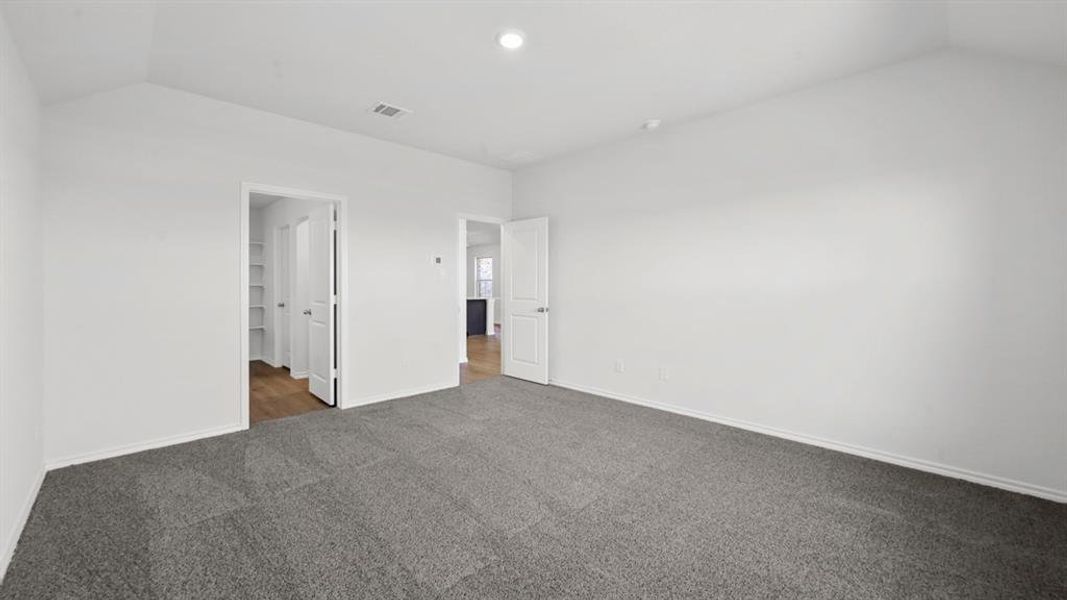 Spacious interior room with neutral gray carpeting, white walls, and a vaulted ceiling
