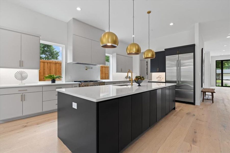 Kitchen with decorative light fixtures, an island with sink, stainless steel appliances, and a healthy amount of sunlight