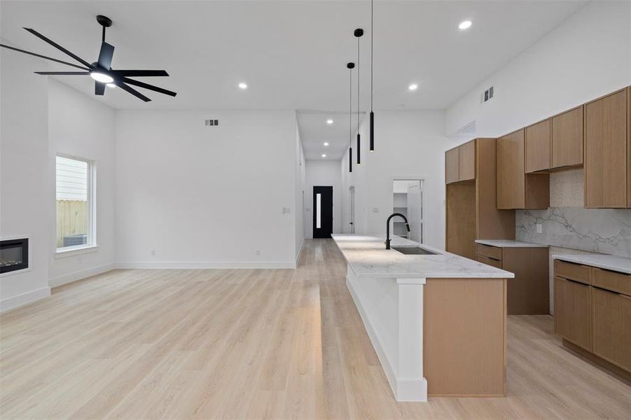 Kitchen featuring light stone countertops, an island with sink, light wood-style floors, pendant lighting, and recessed lighting