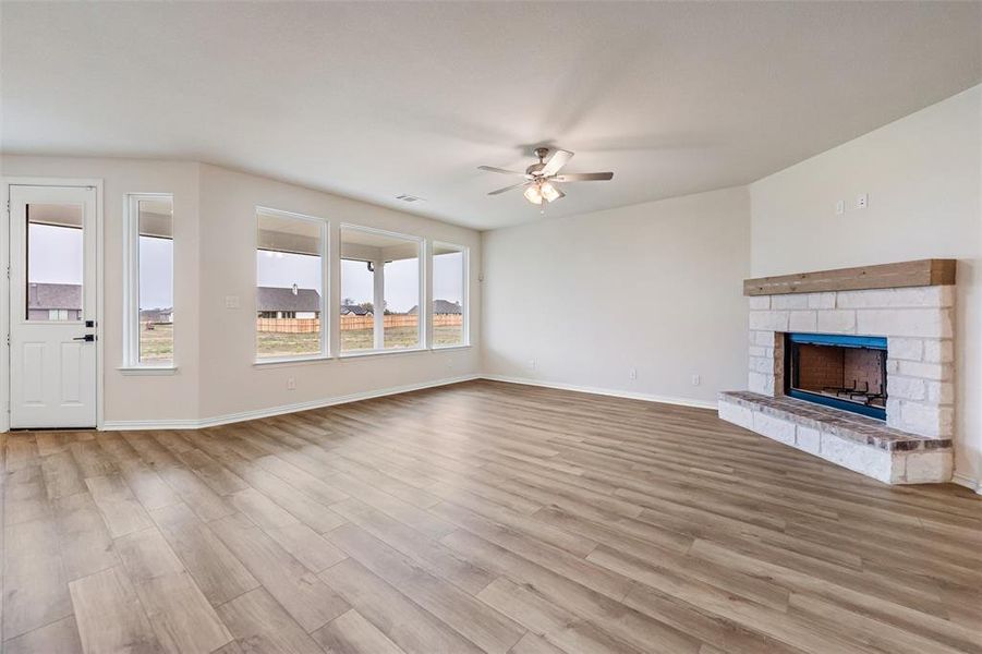 Unfurnished living room featuring a stone fireplace, light wood-style flooring, and ceiling fan