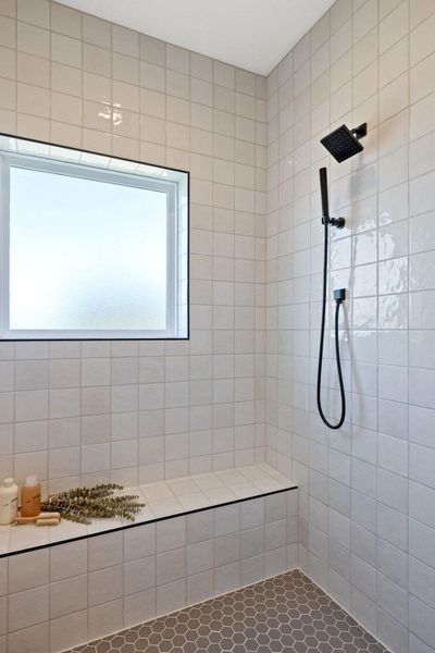 Large walk in shower with bench, dual shower fixture and hand-held wand, shower controls contently located on half wall immediately to the right of the shower door.