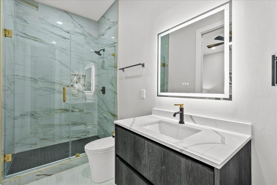 This modern bathroom features a sleek design with a spacious glass-enclosed shower, elegant marble walls, and a stylish vanity with a backlit mirror. The fixtures are contemporary with gold accents, adding a touch of luxury. This modern bathroom features a sleek design with a spacious glass-enclosed shower, elegant marble walls, and a stylish vanity with a backlit mirror. The fixtures are contemporary with gold accents, adding a touch of luxury.