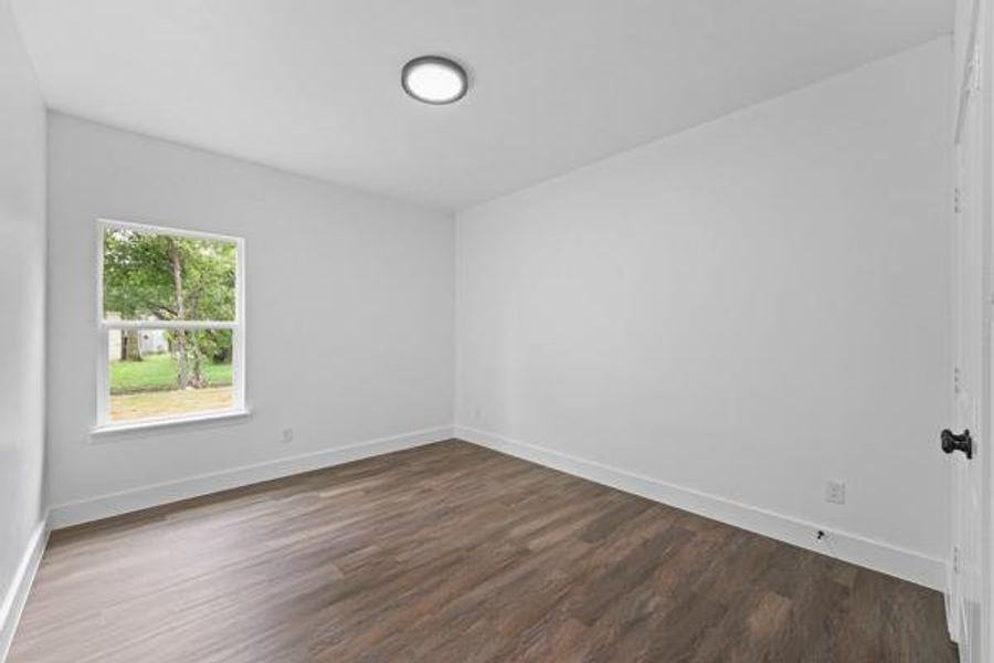 Room featuring wood-finish flooring, white baseboards, a single window, and a flush-mount ceiling light Room featuring wood-finish flooring, white baseboards, a single window, and a flush-mount ceiling light