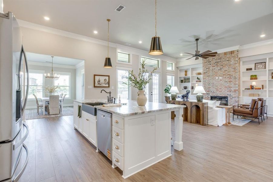 Open-concept living space featuring wood-finish flooring, a kitchen island with stone countertop and farmhouse sink, a brick fireplace, built-in shelving, and recessed lighting