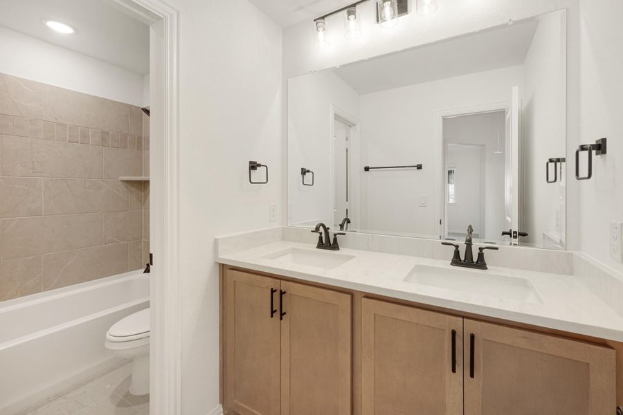 Bathroom with double vanity, wood cabinets, white countertop, large mirror, and tiled tub-shower combo