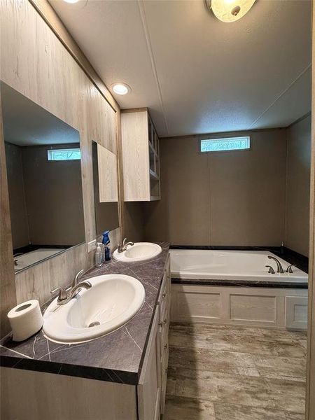 Full bathroom with double vanity, a garden tub, and light wood-type flooring