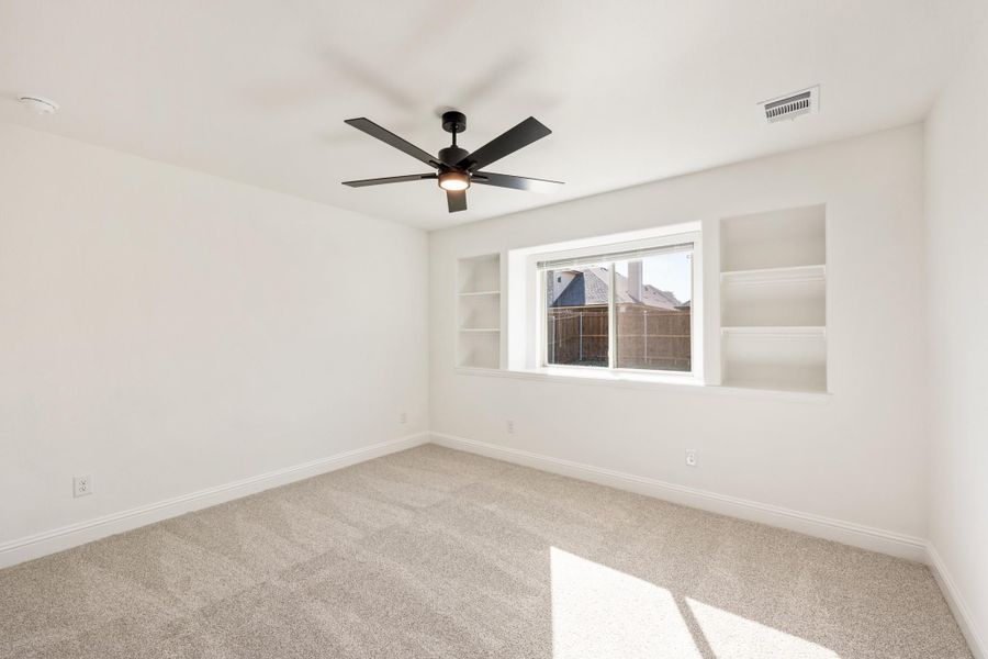 Empty bedroom with carpet, black ceiling fan, built-in shelves, and a window with backyard view