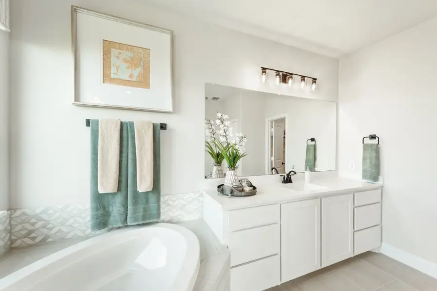 Bathroom with white vanity, large mirror, soaking tub, and tiled surround