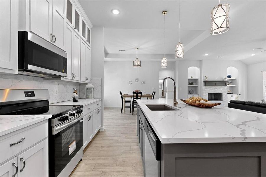 Kitchen with appliances with stainless steel finishes, pendant lighting, light stone counters, glass insert cabinets, and a fireplace Kitchen with appliances with stainless steel finishes, pendant lighting, light stone counters, glass insert cabinets, and a fireplace