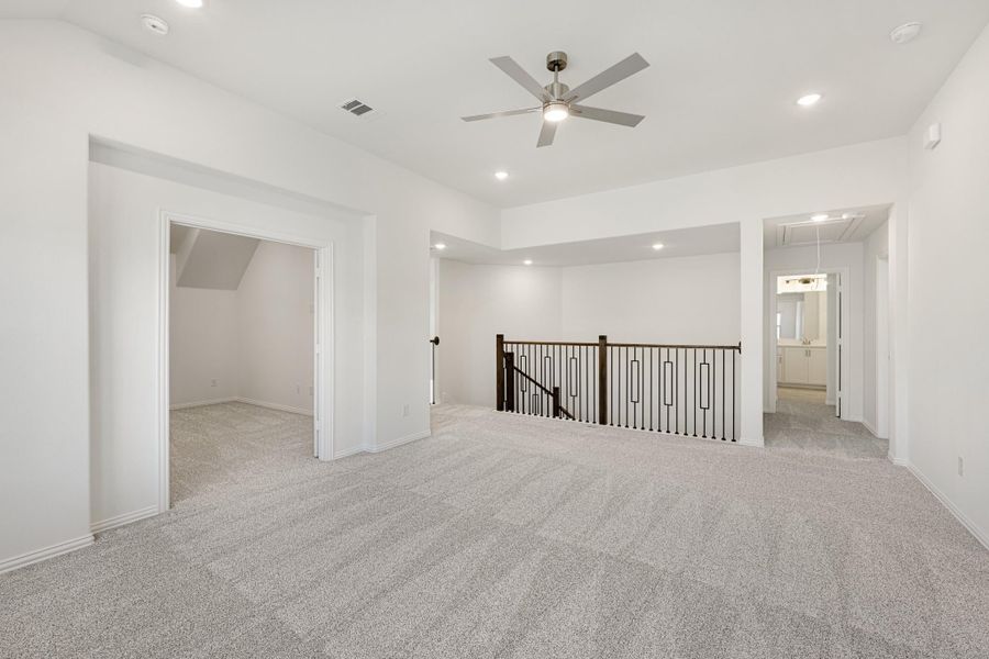Open upstairs loft with carpet, ceiling fan, iron stair railing, and access to bathroom and storage room Open upstairs loft with carpet, ceiling fan, iron stair railing, and access to bathroom and storage room