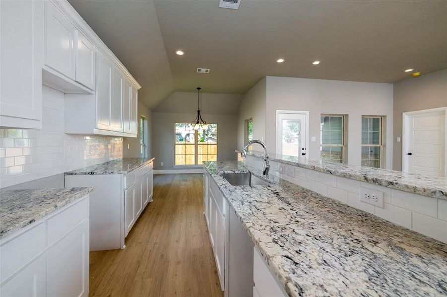 Kitchen with tasteful backsplash, light wood-type flooring, white cabinets, vaulted ceiling, and sink