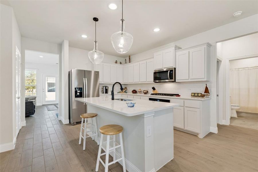 Kitchen featuring a kitchen breakfast bar, white cabinets, stainless steel appliances, light wood-style floors, and pendant lighting, refrigerator will convey with the property Kitchen featuring a kitchen breakfast bar, white cabinets, stainless steel appliances, light wood-style floors, and pendant lighting, refrigerator will convey with the property