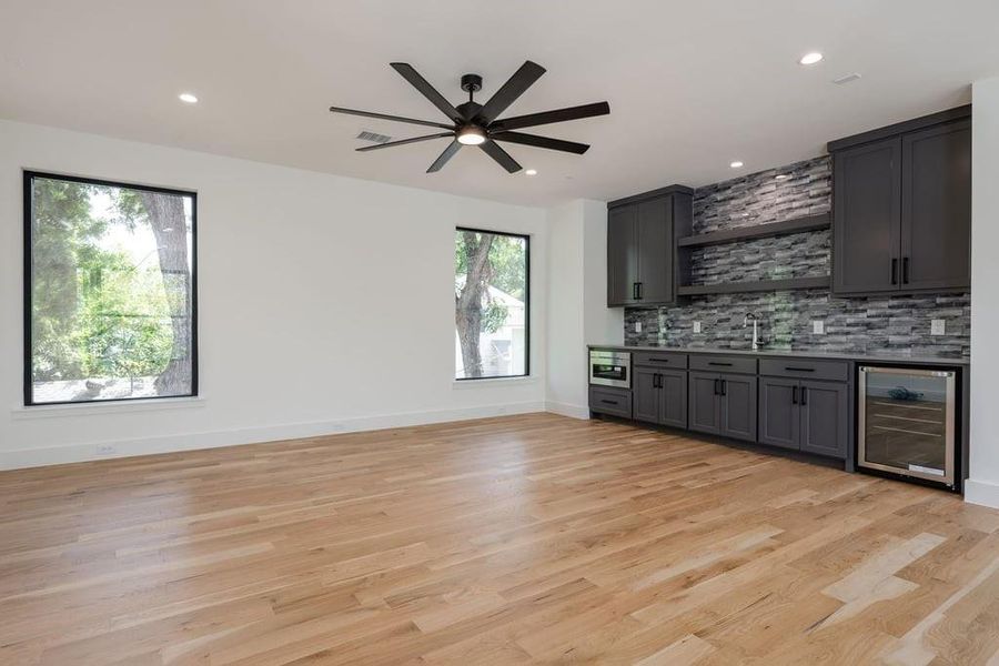 Game room with ceiling fan, decorative backsplash, light hardwood floors, wet bar, microwave and beverage cooler