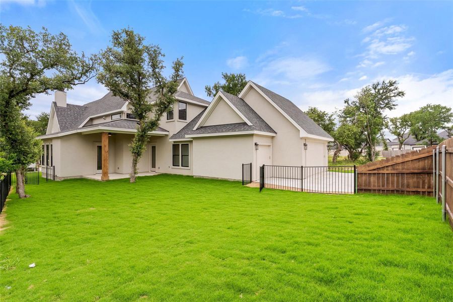 A spacious backyard with mature trees complements the modern stucco home, offering ample green space and a private fenced area.