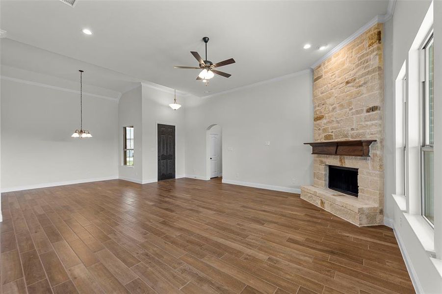 Unfurnished living room with ceiling fan, a stone fireplace, a towering ceiling, and crown molding