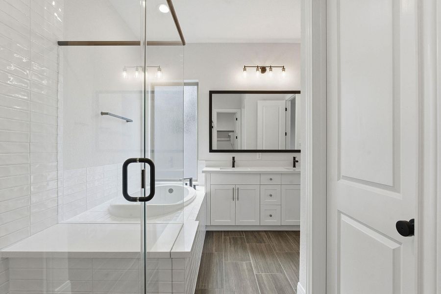 Bathroom featuring double vanity, a shower stall, a bath, and wood finish floors