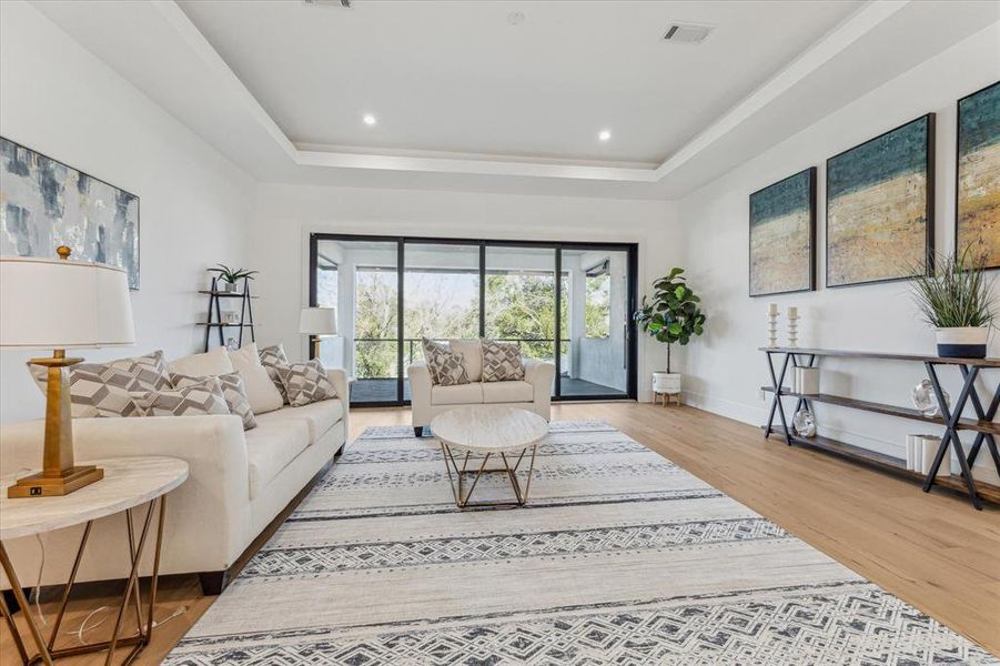 This game room features a spacious layout with light wood flooring, recessed lighting, and a coffered ceiling. Large sliding glass doors lead to an outdoor balcony, providing natural light and seamless indoor-outdoor connectivity.