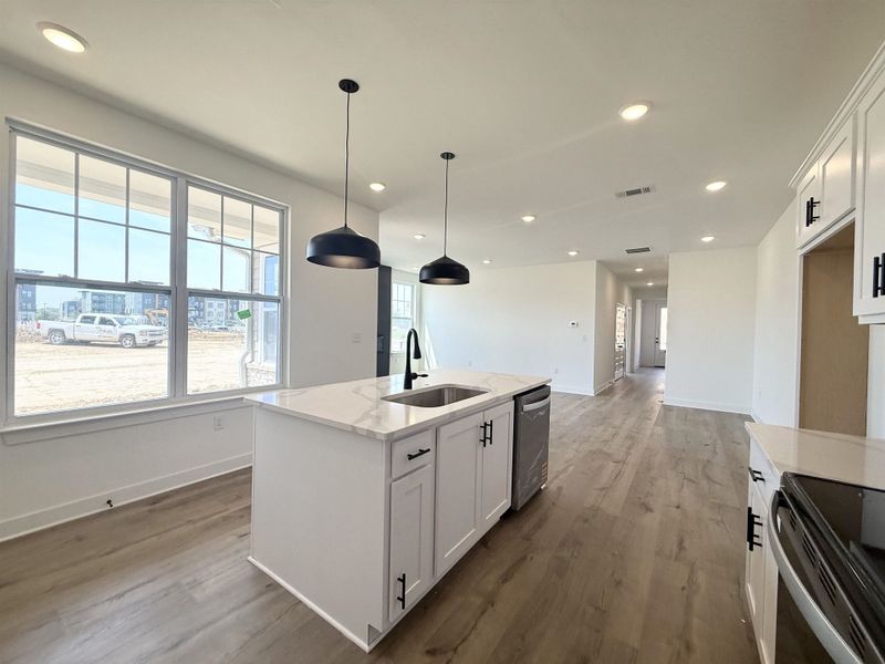 Kitchen featuring a kitchen island with sink, white cabinetry, light stone counters, dark wood finished floors, and pendant lighting