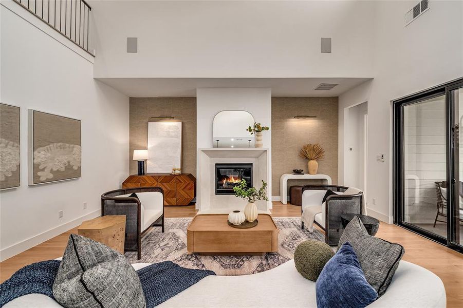 Living room featuring light wood-type flooring, a towering ceiling, and a glass covered fireplace Living room featuring light wood-type flooring, a towering ceiling, and a glass covered fireplace