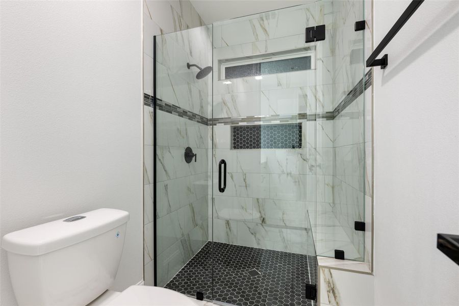 Full bathroom featuring toilet and a marble finish shower