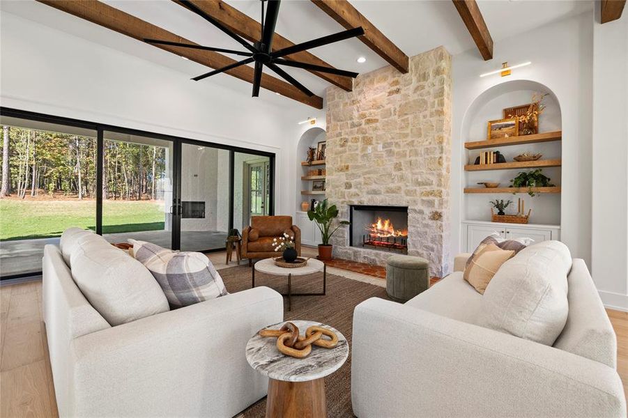 Living room with wood finished floors, built in features, a stone fireplace, beamed ceiling, and ceiling fan