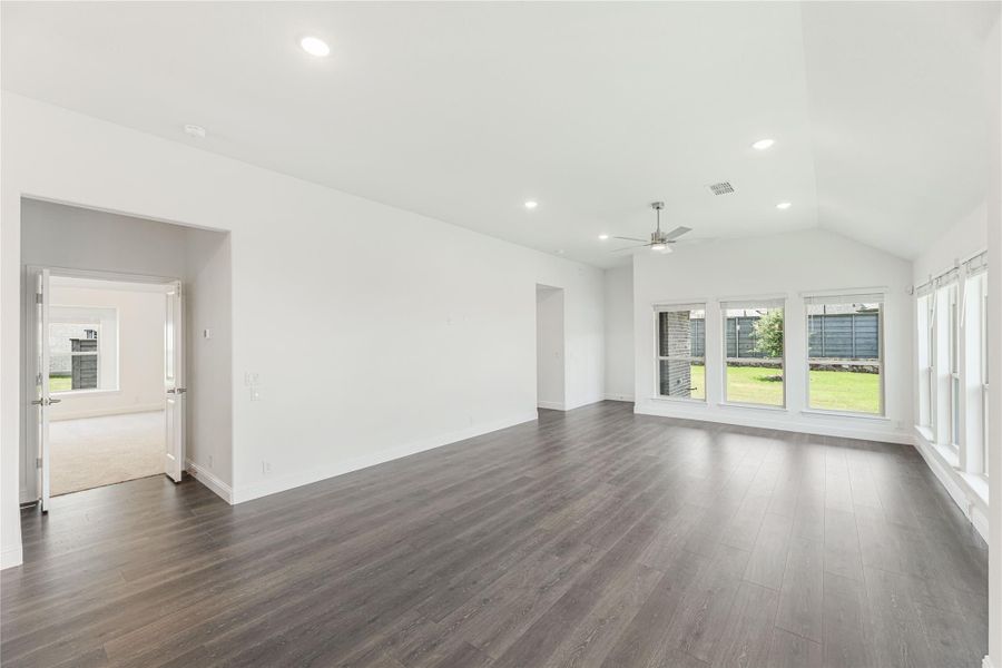 Open living room with vaulted ceiling, dark hardwood floors, ceiling fan, and large windows overlooking backyard Open living room with vaulted ceiling, dark hardwood floors, ceiling fan, and large windows overlooking backyard