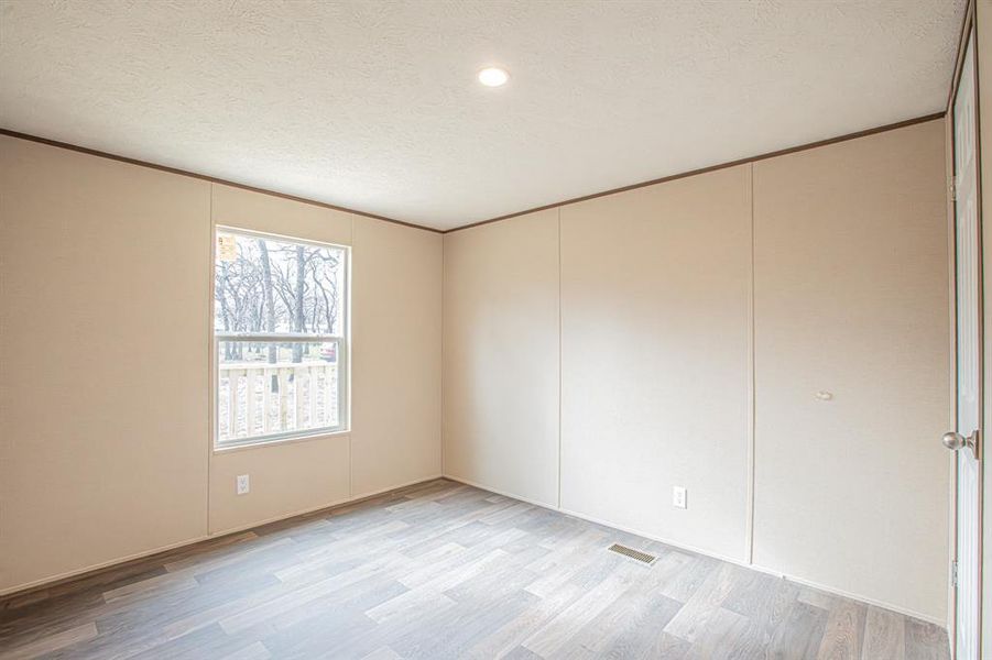 Empty room featuring a textured ceiling, light hardwood / wood-style flooring, and crown molding Empty room featuring a textured ceiling, light hardwood / wood-style flooring, and crown molding