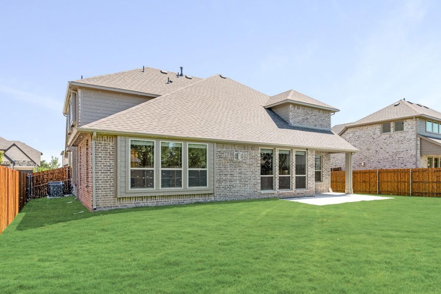 Brick home rear exterior with large windows, concrete patio, and fenced backyard with green lawn Brick home rear exterior with large windows, concrete patio, and fenced backyard with green lawn