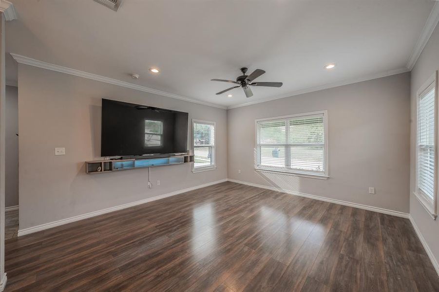 Unfurnished living room with crown molding, dark wood-style flooring, healthy amount of natural light, a ceiling fan, and recessed lighting Unfurnished living room with crown molding, dark wood-style flooring, healthy amount of natural light, a ceiling fan, and recessed lighting