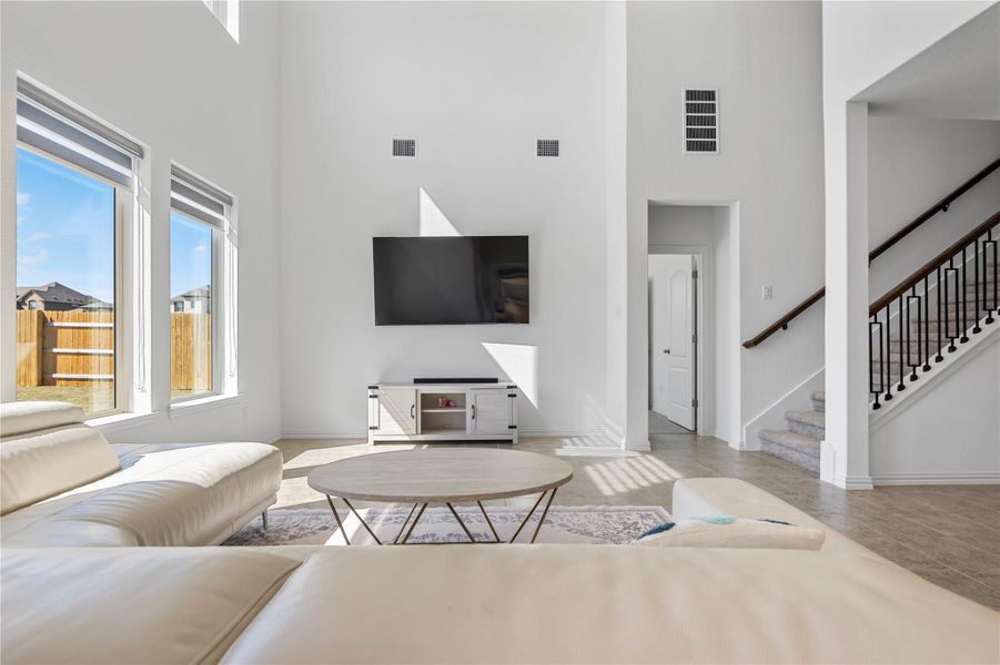 A spacious living room features soaring ceilings, large windows, and a carpeted staircase with an elegant railing leading to the upper level. A spacious living room features soaring ceilings, large windows, and a carpeted staircase with an elegant railing leading to the upper level.