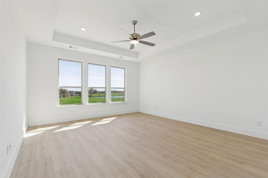 Spare room featuring a raised ceiling, light wood-style floors, a ceiling fan, and recessed lighting
