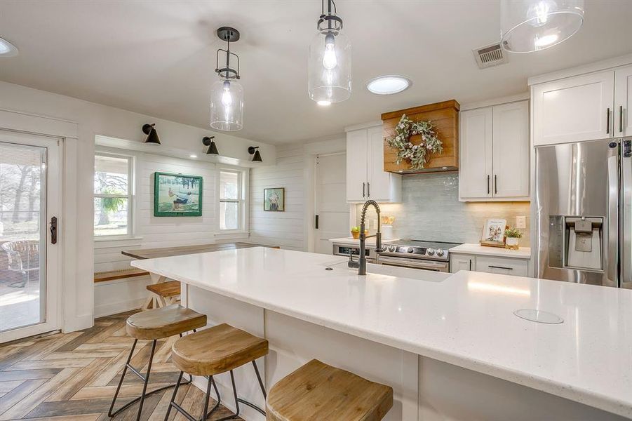 Kitchen with white cabinetry, stainless steel appliances, decorative light fixtures, parquet floors, and a breakfast bar