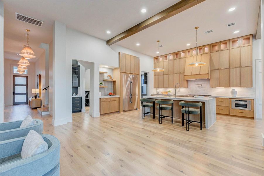 The gourmet kitchen impresses with a dramatic waterfall island wrapped in quartz, pendant lighting, and full-height cabinetry with display windows. Natural wood cabinetry and sleek brass hardware create a timeless, upscale aesthetic.