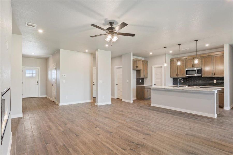 Kitchen with tasteful backsplash, pendant lighting, open floor plan, ceiling fan, and a center island with sink