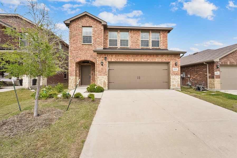 Two-story brick exterior featuring a stone accent façade, an arched entryway, a two-car garage, and a concrete driveway
