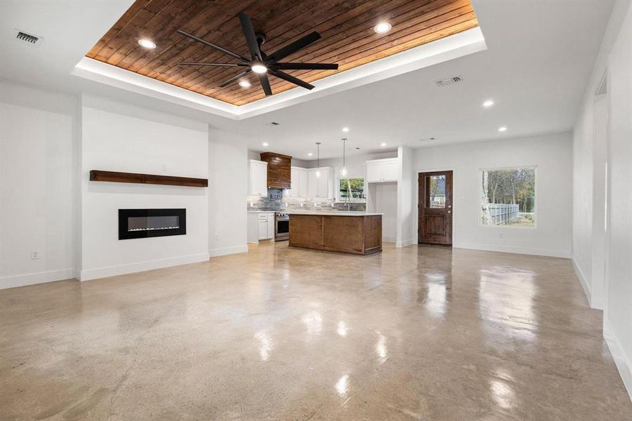 Unfurnished living room featuring wood ceiling, a glass covered fireplace, a tray ceiling, concrete floors, and a ceiling fan