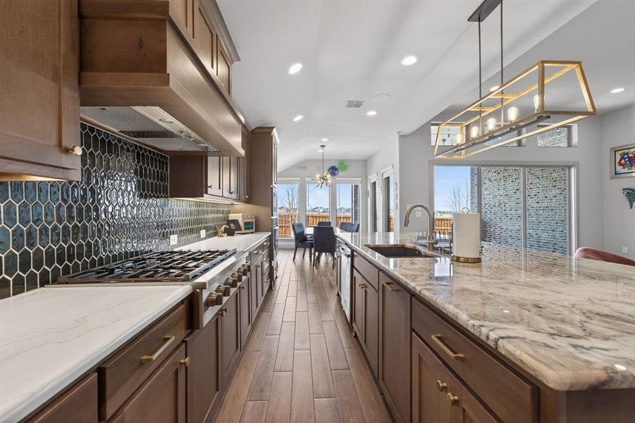 Kitchen with stainless steel gas cooktop, light stone counters, backsplash, and a large island Kitchen with stainless steel gas cooktop, light stone counters, backsplash, and a large island