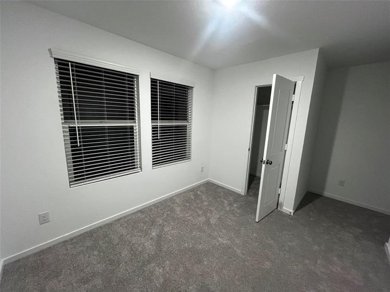 Room featuring two windows with white blinds, light gray carpet, white walls, and a white interior door with a black doorknob Room featuring two windows with white blinds, light gray carpet, white walls, and a white interior door with a black doorknob
