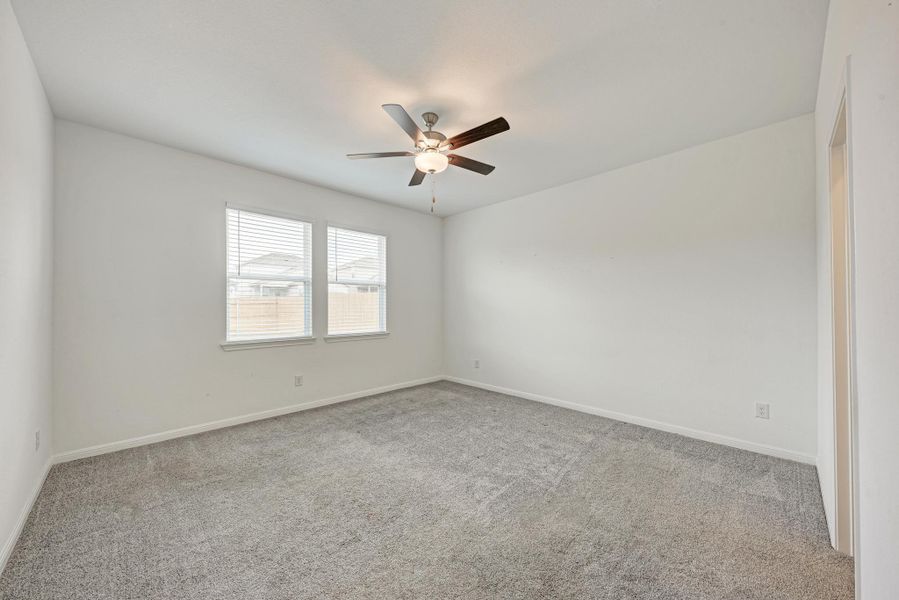 A spacious bedroom features two sun-filled windows, plush carpet flooring, and an overhead ceiling fan.