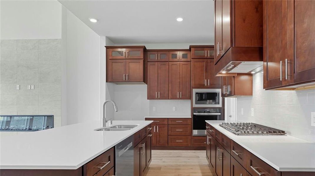 Kitchen featuring stainless steel appliances, glass fronted cabinets, light wood-style floors, tasteful backsplash, and recessed lighting