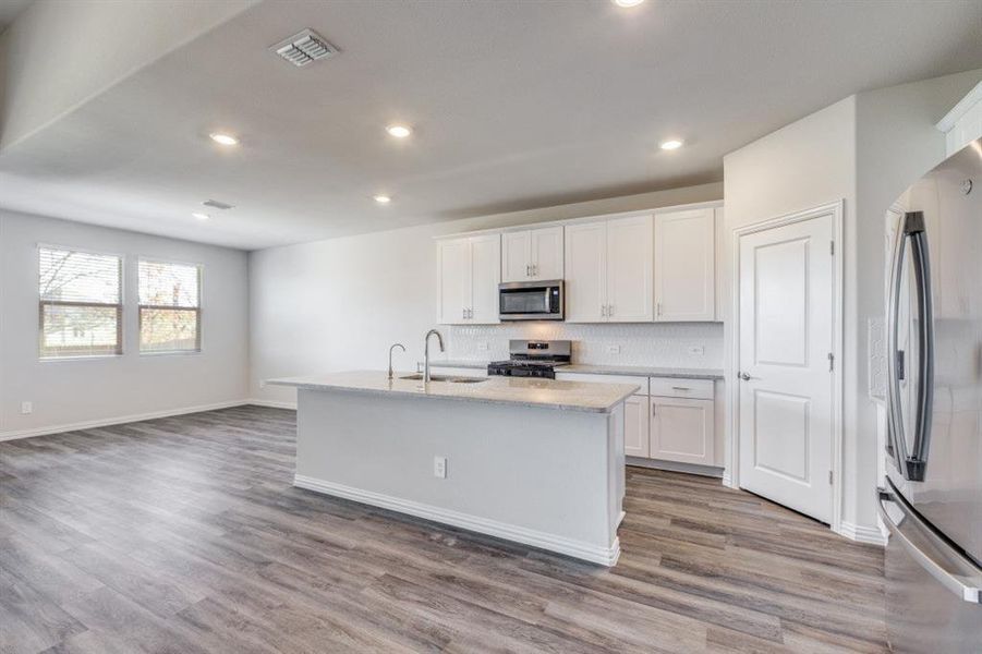 Kitchen with a kitchen island with sink, white cabinets, appliances with stainless steel finishes, backsplash, and light wood-style floors