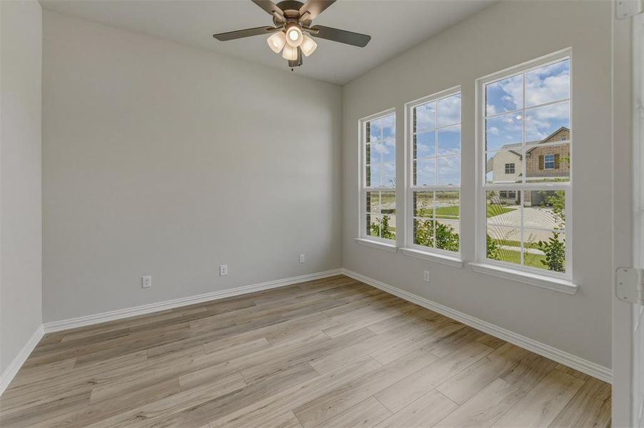 Room with three large windows, wood-finish flooring, and a ceiling fan Room with three large windows, wood-finish flooring, and a ceiling fan