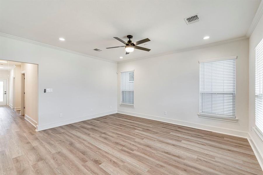 Empty room with light wood-style flooring, baseboards, visible vents, ceiling fan, and ornamental molding Empty room with light wood-style flooring, baseboards, visible vents, ceiling fan, and ornamental molding